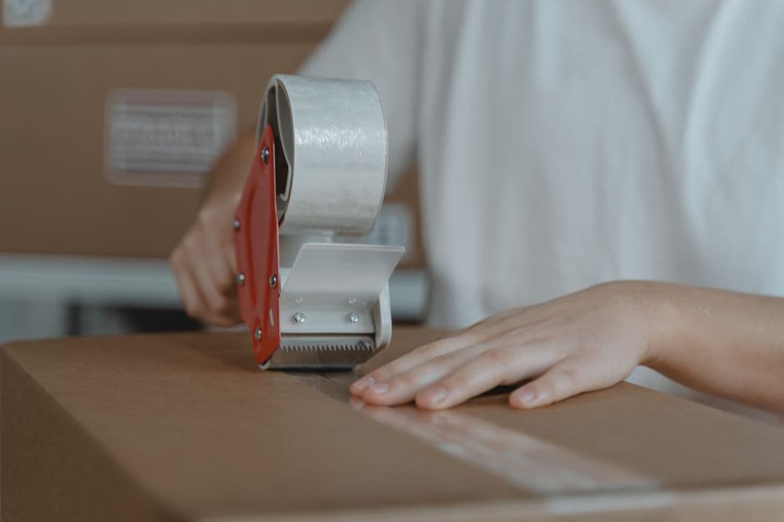 Person sealing a cardboard box with tape before sending