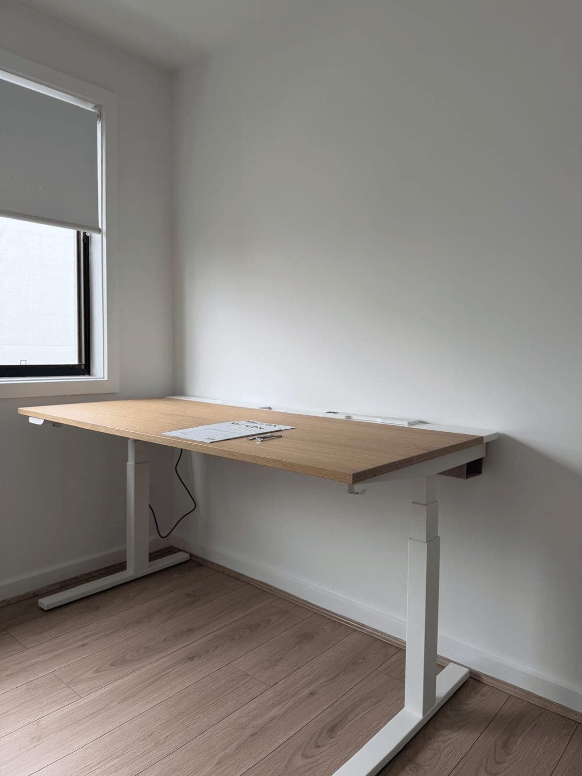 IKEA electric sit-stand desk with an oak top and white frame, assembled in a corner of an empty room