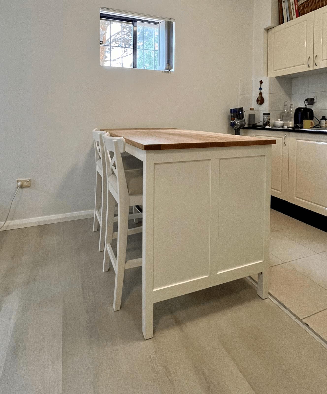 White kitchen island with a solid oak top and two white cross-back bar stools, assembled by Liztty in a kitchen