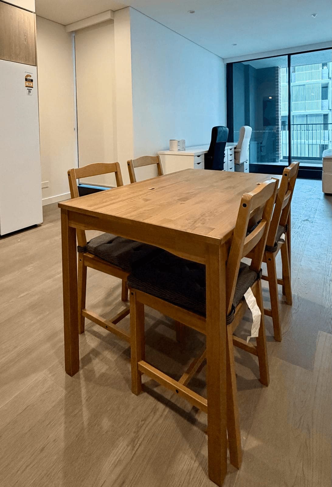 Pine dining table with four matching chairs and seat cushions, assembled in an apartment beside the kitchen