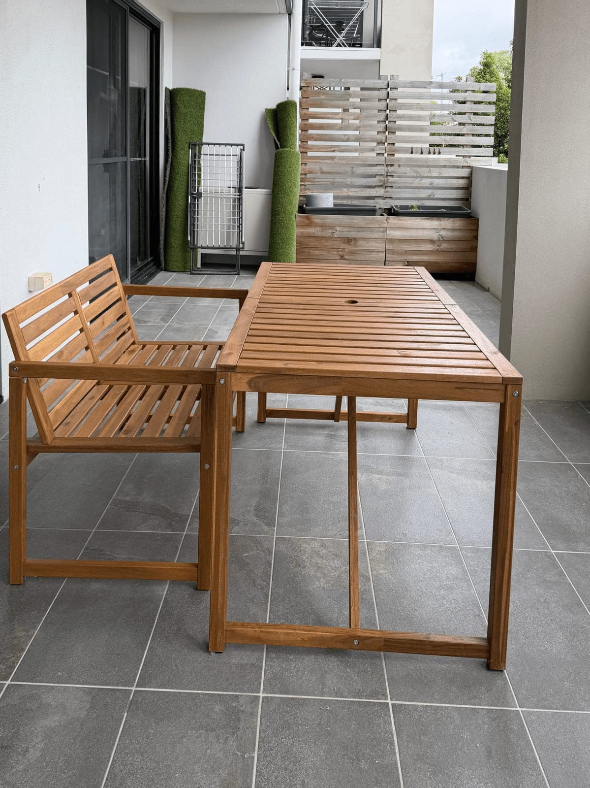 Acacia timber outdoor dining table with a slatted top and matching bench seat, assembled on a tiled balcony