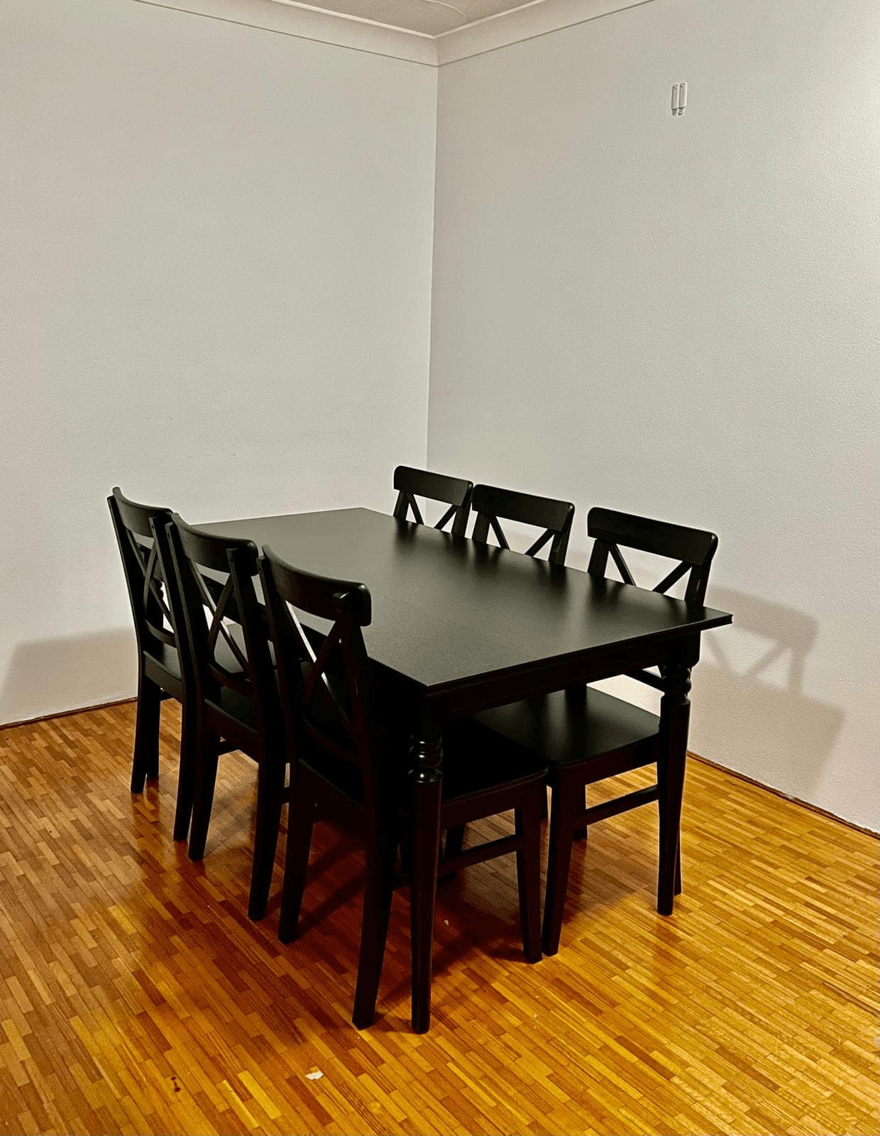 Black dining table with five cross-back chairs and a matching bench, assembled on parquet flooring