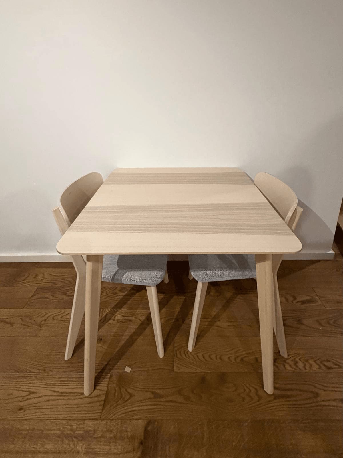 Small light ash IKEA dining table with two curved-back chairs, assembled against a wall on timber flooring