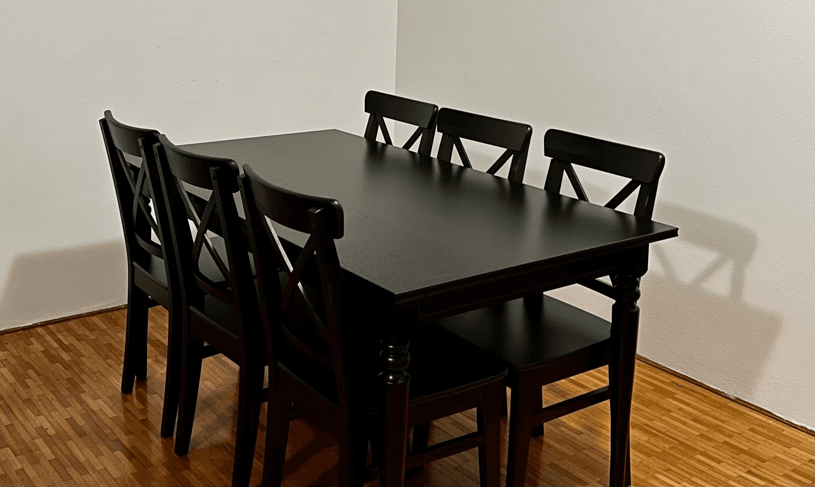 Black timber dining table with six matching cross-back chairs, assembled by Liztty on a timber floor against a white wall