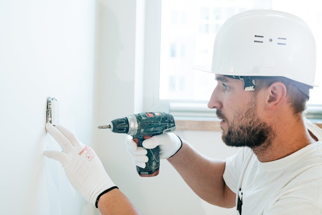 Professional handyman with hard hat using a power drill on a wall