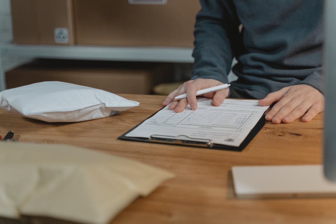 Person filling in delivery details on a clipboard with boxes nearby
