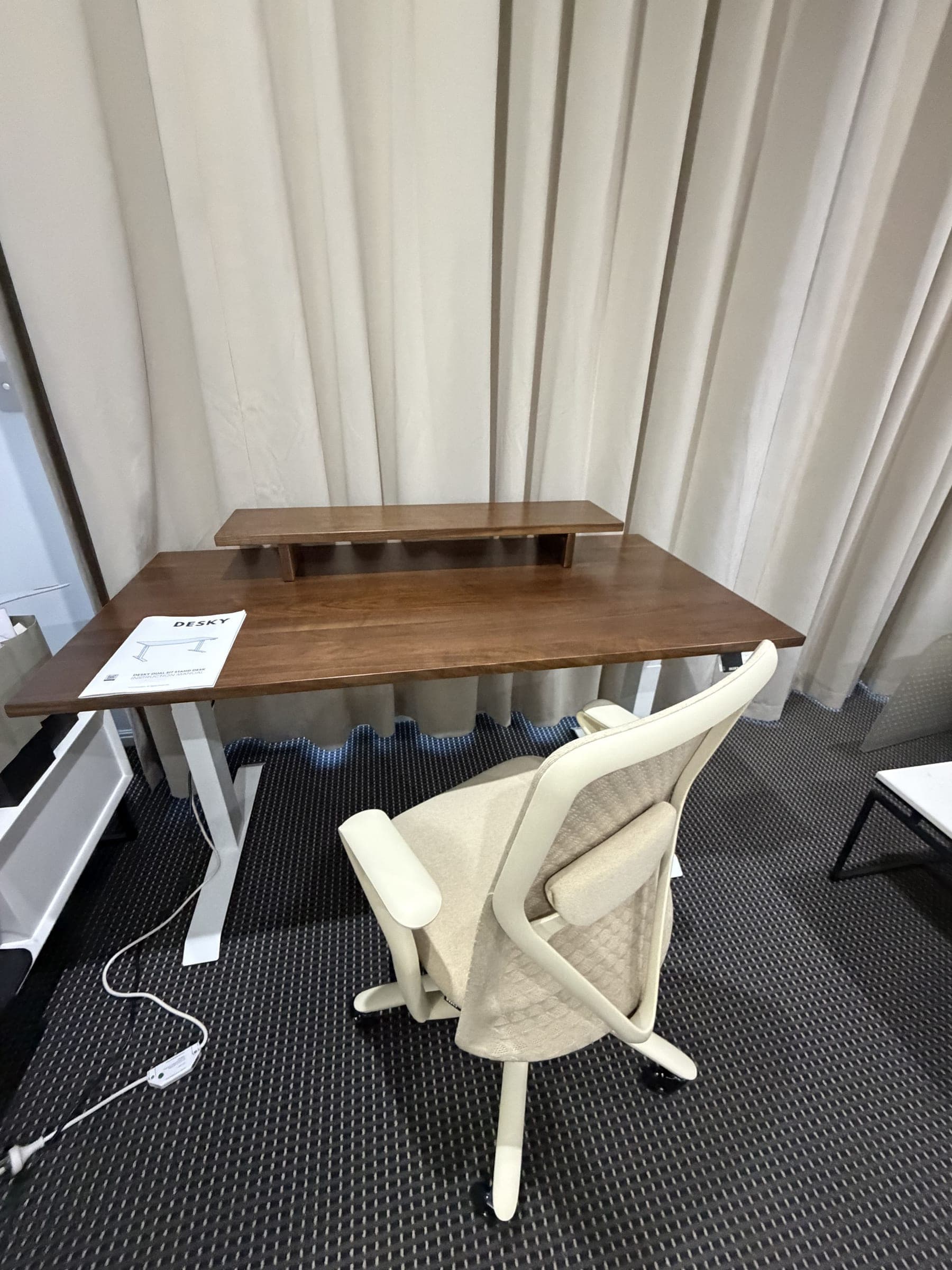 Assembled Desky dual sit-stand desk with a walnut top, white electric frame and monitor riser, with the instruction manual still on the desk