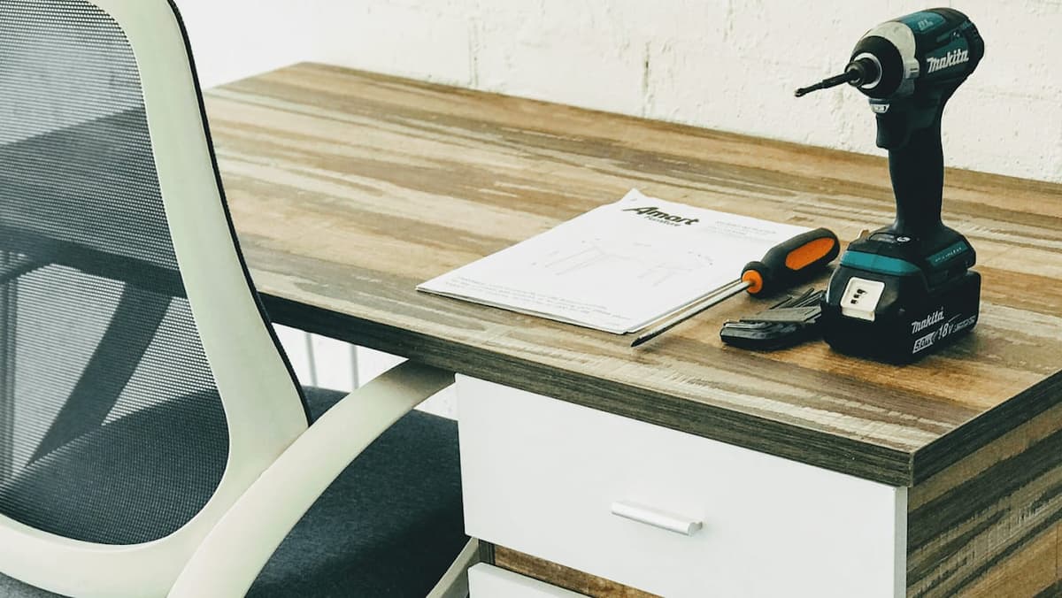 Assembled desk with drawers, with an Amart Furniture instruction sheet, impact driver, screwdriver and hex keys left on top