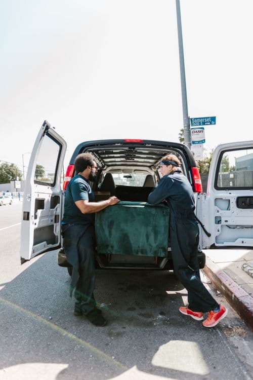 Two removal workers loading furniture into a van