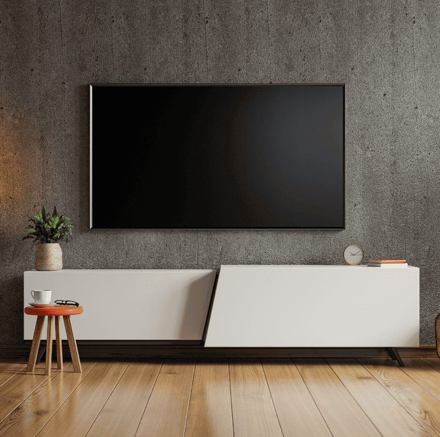 A flat-screen TV mounted on a raw concrete wall above a low white cabinet, in a room with timber flooring